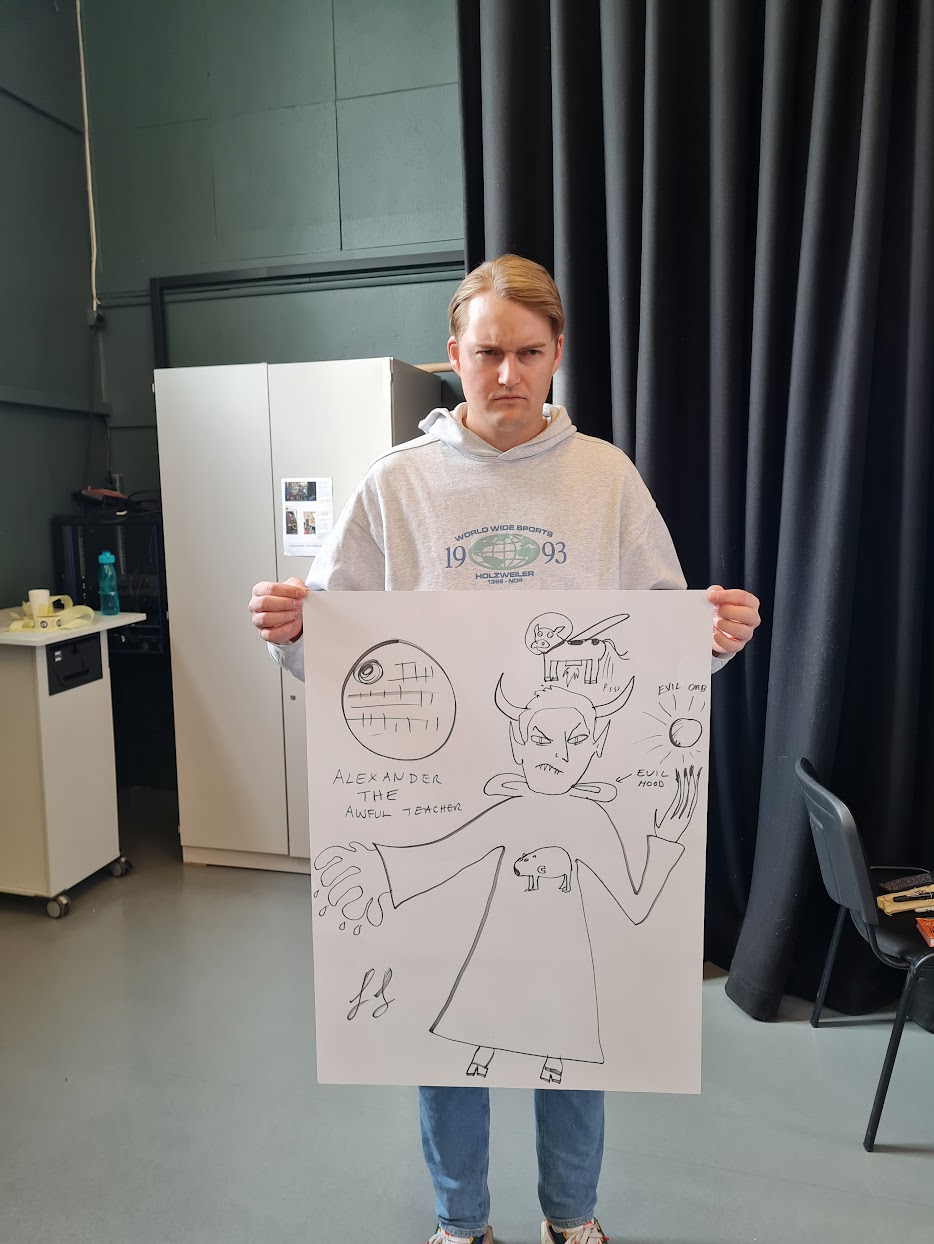 A blond teacher in a hoody scowling and holding up a parody picture of him as an evil god.